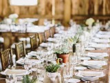 a simple and neutral barn wedding tablescape with a table runner of potted greenery and succulents, neutral linens and menus