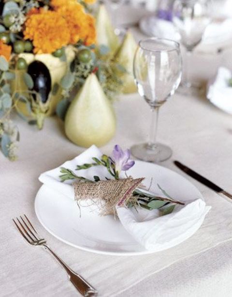a fall barn wedding tablescape with neutral linens, a lush fruit, veggie and floral centerpiece and a burlap napkin ring