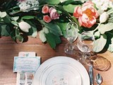 a chic and fresh wedding barn tablescape with an uncovered table, a greenery and pink bloom runner, bright stationery