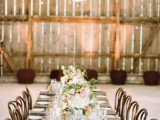 a barn wedding tablescape with an uncovered table, a white table runner, white and pink blooms and greenery for a refined touch