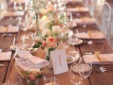a romantic barn wedding table setting with an uncovered table, a burlap table runner, peachy and white blooms, white linens