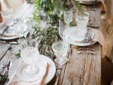 a simple barn wedding table setting with an uncovered table, greenery and a greenery and white bloom centerpiece and white linens