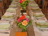 a bright rustic wedding tablescape with a burlap table runner, bright blooms and greenery, vintage books and colorful napkins