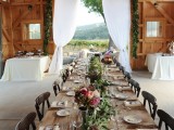a barn wedding table setting with an uncovered table, a greenery table runner, bright blooms and neutral linens