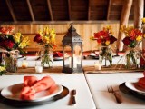 a colorful vintage barn wedding tablescape with bright floral centerpieces, a candle lantern, a burlap table runner and bright napkins