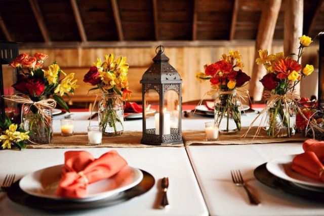 A colorful vintage barn wedding tablescape with bright floral centerpieces, a candle lantern, a burlap table runner and bright napkins