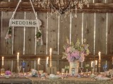 a vintage pastel barn wedding table with pastel florals, colored glasses, candles and votives and a lace table runner
