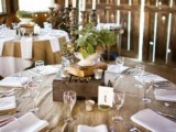 a cool barn wedding tablescape with a burlap tablecloth, white napkins, a box and a book on top and a greenery centerpiece