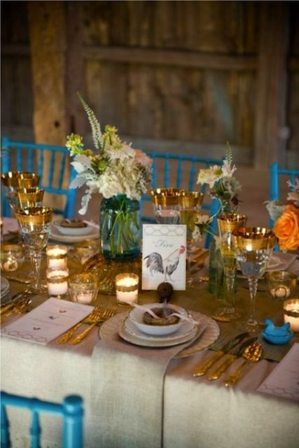 a bright barn wedding table with a burlap runner, neutral napkins, gold cutlery and gold rimmed glasses, neutral blooms and votives