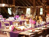 a bright beautiful wedding tablescape with a purple table runner, bright blooms, branches with crystals and lights around