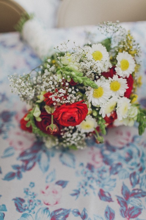 a bright summer wedding bouquet of hot red ranunculus, white chamomiles, baby's breath and greenery for a relaxed summer wedding