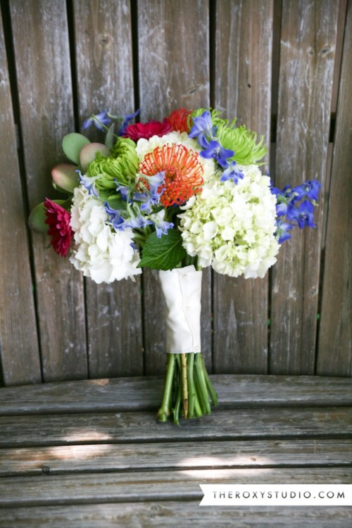 a bright summer wedding of white hydrangeas, orange pincushion proteas, purple blooms and greenery for summer