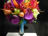 a colorful tropical wedding bouquet of orange, green, deep purple, red blooms and some greenery is a bold color statement