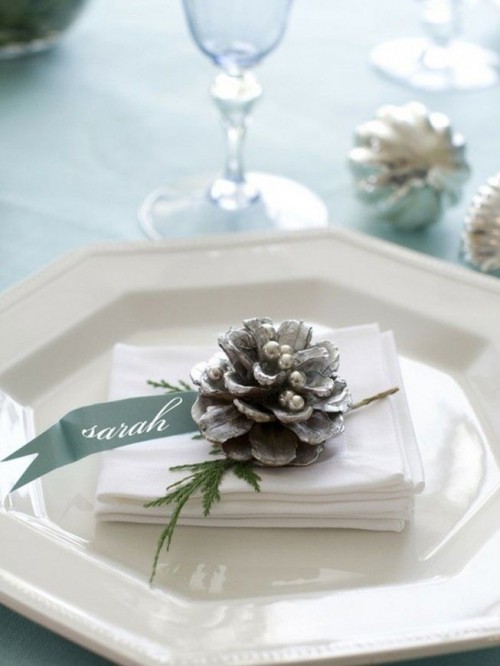 a neutral winter place setting with a geometric plate, pinecones with pearls, greenery and ribbons