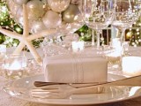 a beautiful white and mother of pearl wedding tablescape with a textural tablecloth, beads, candles, a centerpiece of neutral ornaments