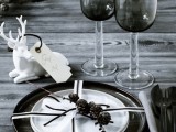 a moody Christmas tablescape with a naked table, dark and white porcelain, dark glasses and a deer figurine as a favor
