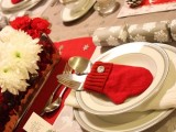 a cozy neutral and red Christmas tablescape with printed placemats and runners, a red and white bloom centerpiece, a snowflake napkin and a red mitted cutlery pocket