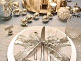 a bright metallic Christmas tablescape with metallic ornaments, mercury glass candleholders, a bottle and candles centerpiece and a silver ribbon bow