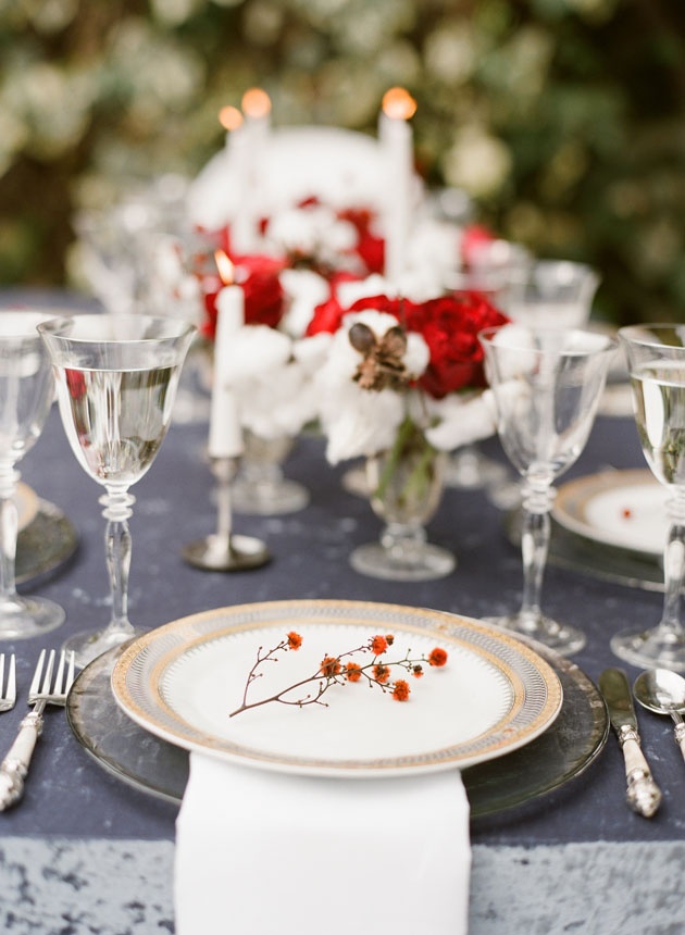 A chic grey and red Christmas tablescape with red and white blooms, marble chargers, berries and sivler cutlery and silver glasses