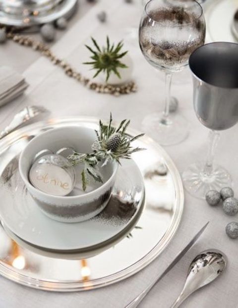 a neutral Christmas tablescape with thostles, glitter ornaments, grey and sivler plates, sheer white ornaments with names