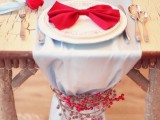 a natural Christmas tablescape with a grey table runner decorated with red berries, plates with red bows and silver cutlery