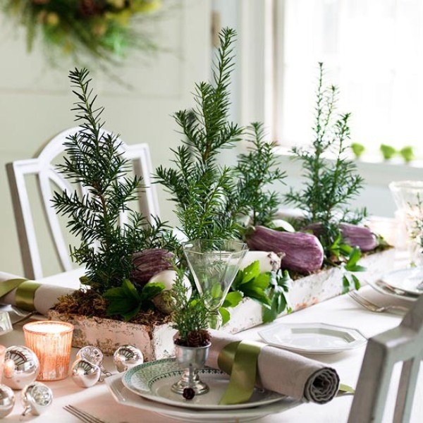 A natural Christmas tablescape with Christmas trees, a box centerpiece with veggies and greenery, metallic ornaments and candles, pinecones and evergreens in cups