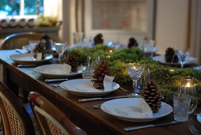 A natural Christmas table with moss and candles, pinecones, white porcelain and elegant glasses
