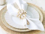 a gold and white Christmas tablescape with gold chargers and snowflake napkin rings, mercury glass candleholders and white napkins