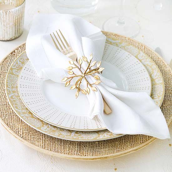 A gold and white Christmas tablescape with gold chargers and snowflake napkin rings, mercury glass candleholders and white napkins