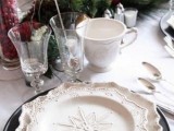 a refined Christmas wedding table with black chargers and white snowflake plates, evergreens and apples, candles and cranberries in vases