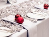 a grey and white Christmas tablescape spruced up with red ornaments and silver cutlery