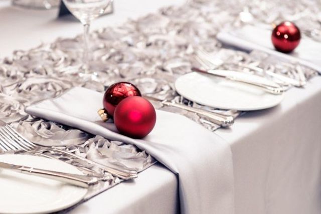 A grey and white Christmas tablescape spruced up with red ornaments and silver cutlery