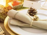 a chic Christmas place setting with moss, candles, apples, a gold charger, a napkin with a pinecone and a bell