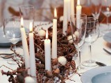 a natural Christmas tablescape with blue plates, dried branches and pinecones, candles and felt snowballs