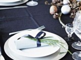 a dark natural tablescape with a black tablecloth, dried branches and acorns, black ribbons and evergreens