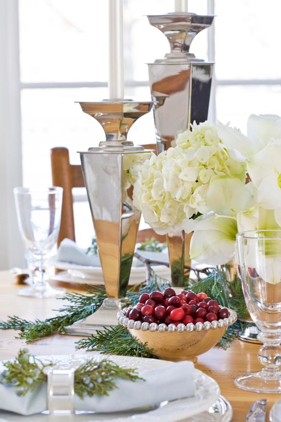 a natural meets glam Christmas table setting with large shiny vases, white blooms, evergreens, cranberries and shiny napkin rings