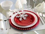 a red and white Christmas tablescape with silver placemats, red plates, snowflakes and faux snow