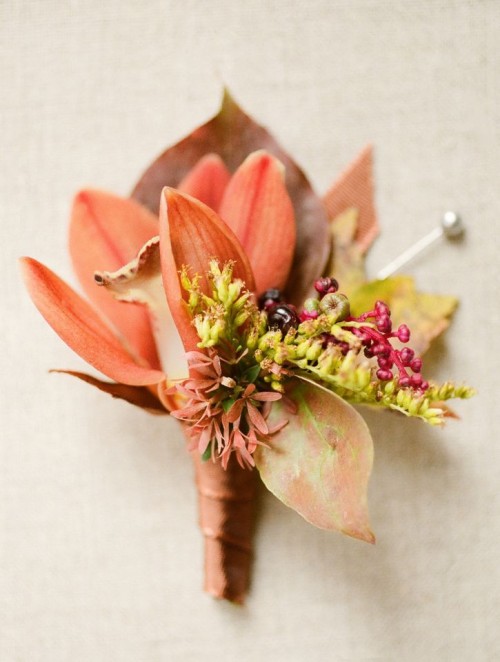 a bold fall wedding boutonniere with a rust-colored lily, berries, greenery, bold leaves and elegant ribbon wrap