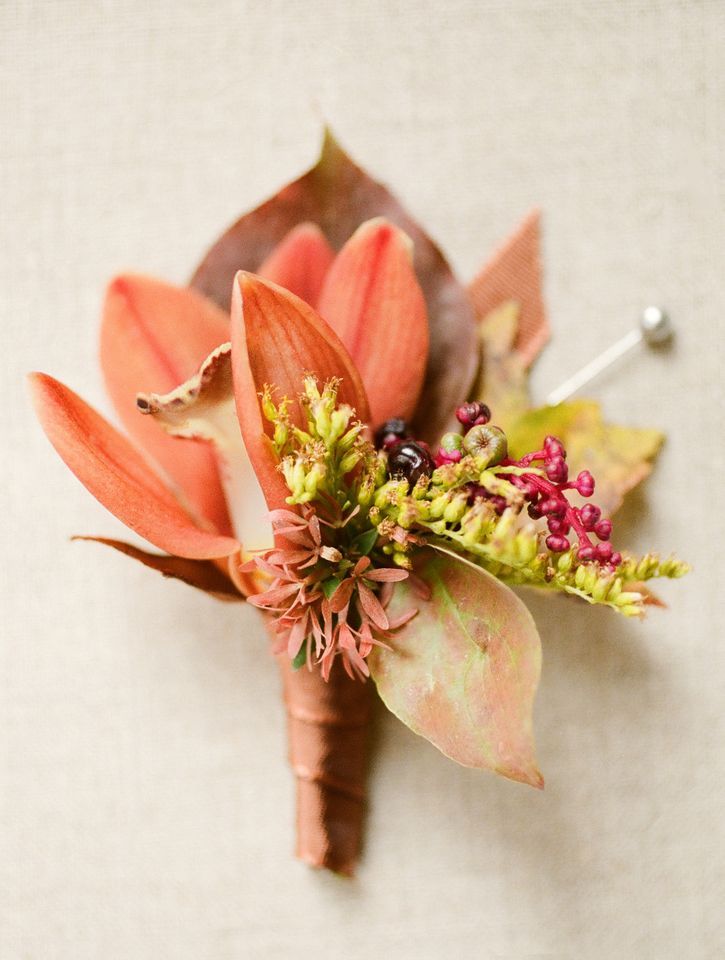 a bold fall wedding boutonniere with a rust colored lily, berries, greenery, bold leaves and elegant ribbon wrap