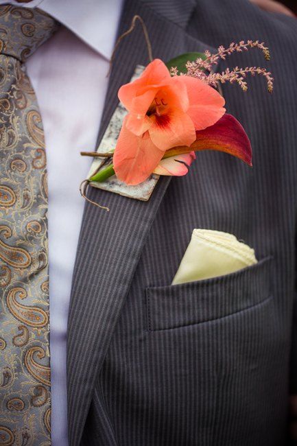 a bright wedding boutonniere with an orange bloom, green and bright leaves and branches for a fall groom