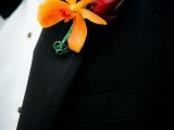a bold and cool wedding boutonniere with orange and deep red blooms plus a leaf for an elegant and chic groom’s look