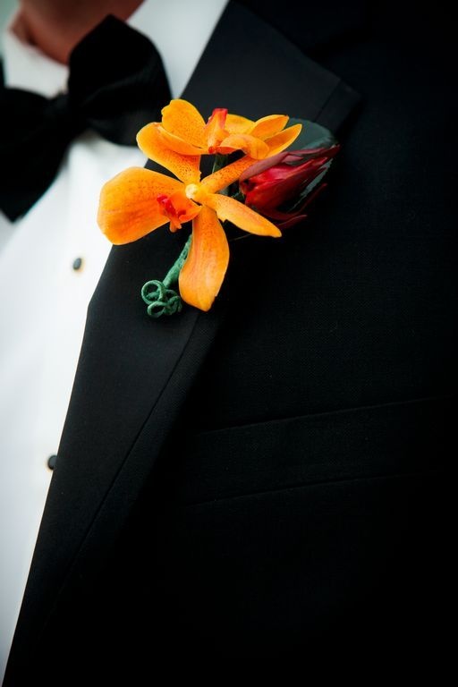 a bold and cool wedding boutonniere with orange and deep red blooms plus a leaf for an elegant and chic groom's look