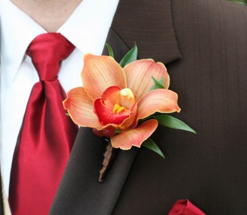 a bold rust-colored wedding boutonniere with greenery and a bright red tie for a chic and bold groom's look
