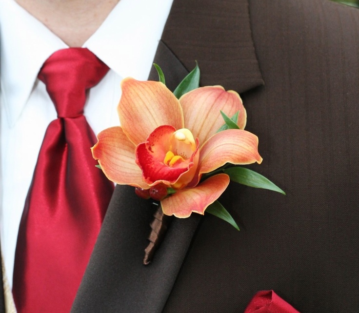 a bold rust colored wedding boutonniere with greenery and a bright red tie for a chic and bold groom's look