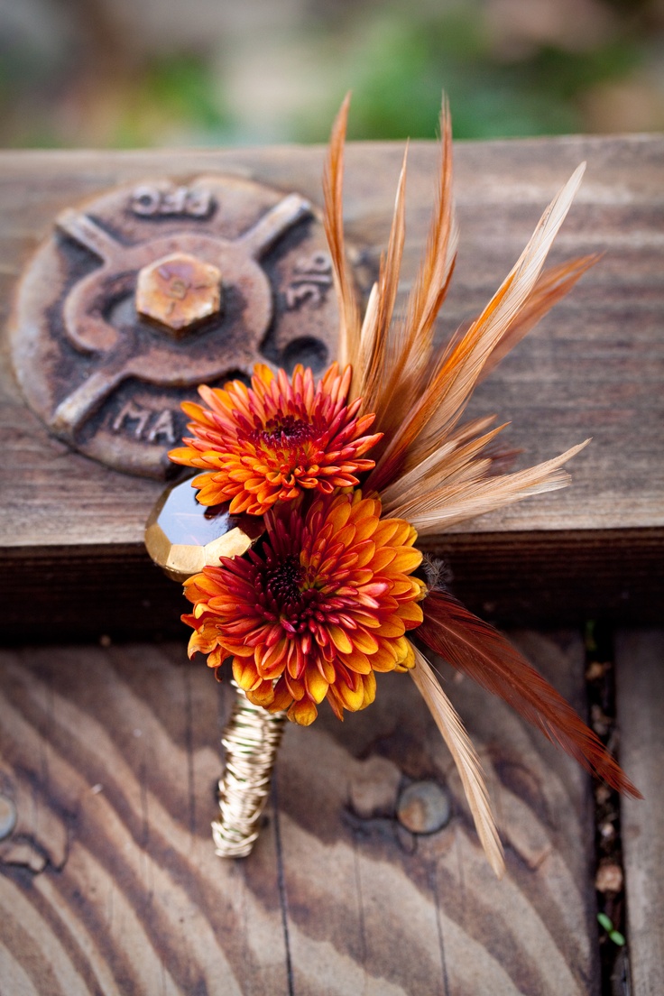 a bright wedding boutonniere with orange blooms, feathers and a bold tan crystal is a chic and bold accessory to rock