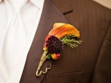 a refined wedding boutonniere with an orange calla, a burgundy bloom and greenery is a cool and bold piece to rock