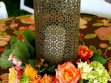an elegant fall wedding centepiece of a laser cut candleholder and greenery and bright blooms around it