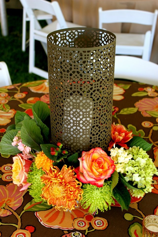 An elegant fall wedding centepiece of a laser cut candleholder and greenery and bright blooms around it