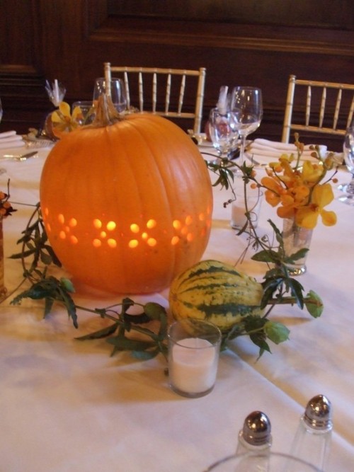 a cutout pumpkin candleholder, some blooms, greenery, a zucchini, candles for a creative fall wedding centerpiece