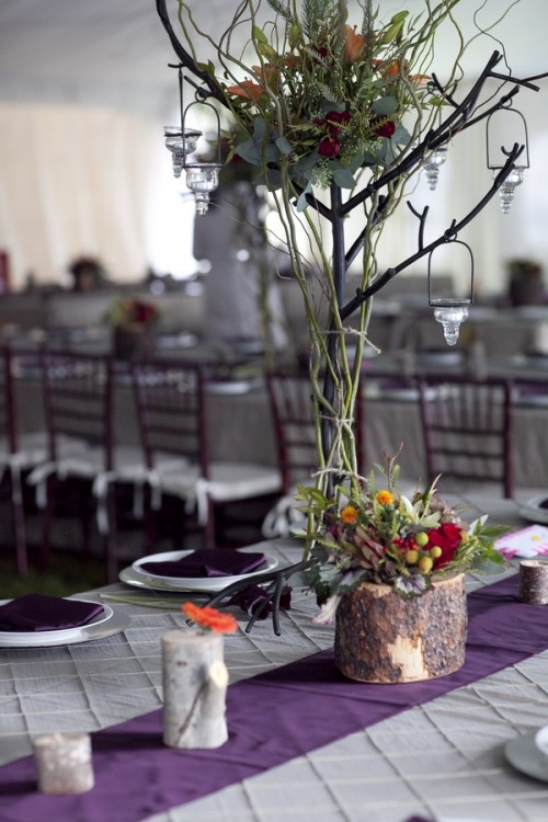 a tall fall wedding centerpiece of branches, greenery, bold blooms, colorful flowers in a tree stump and some candles